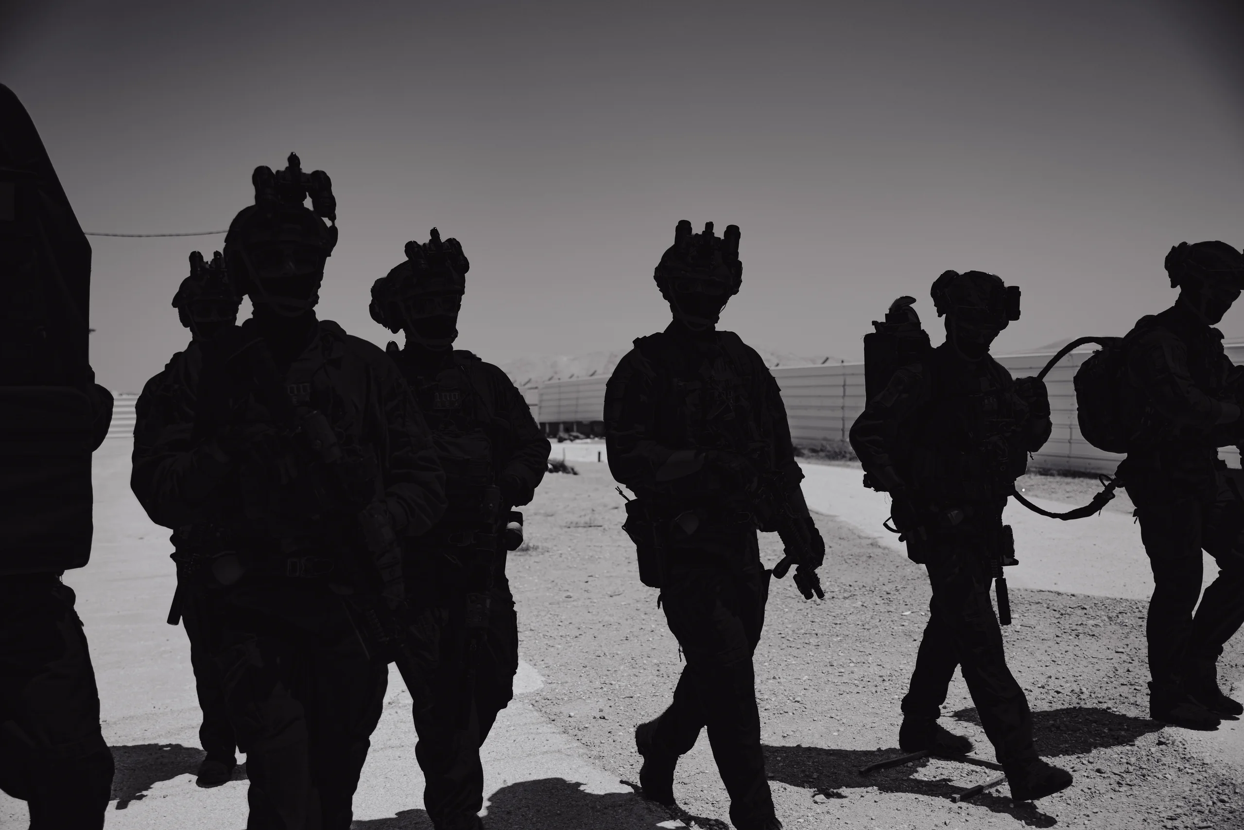 Silhouetted figures in tactical gear walking across desert terrain at low sun